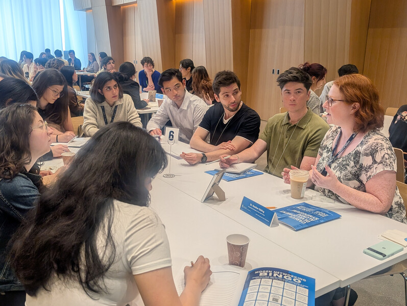 A group of graduate students sit around a table in conversation with an alumni mentor